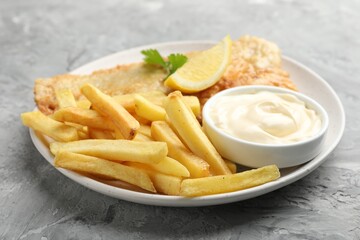 British Traditional Fish and chips with sauce, lemon and parsley on gray textured table, closeup