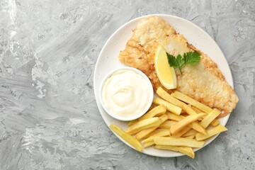 British Traditional Fish and chips with sauce, lemon and parsley on gray textured table, top view. Space for text