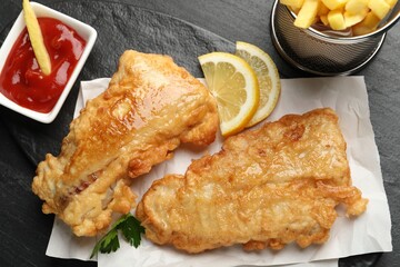 British Traditional Fish and chips with sauce and lemon on dark textured table, top view