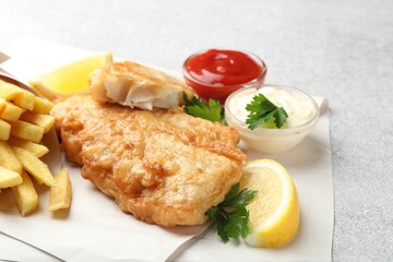 British Traditional Fish and chips served with sauces on light grey table, closeup