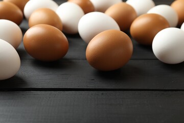 Many raw chicken eggs on black wooden table, closeup. Space for text