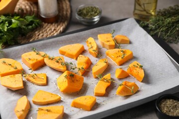 Pieces of fresh pumpkin with thyme and other spices on grey table, closeup