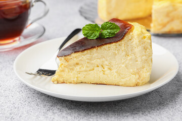 Piece of delicious Basque cheesecake with mint and tea on light grey table, closeup