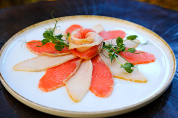 Sashimi slices arranged on a floral-patterned porcelain plate, garnished with fresh wasabi and daikon strips for a refined presentation. oily red fish in slices on a white plate