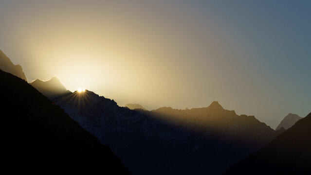 Sunbeams pierce mountain peaks at dawn