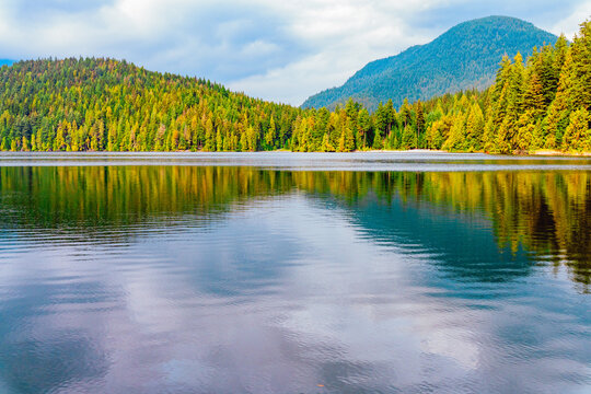 Scenic view across tranquil BC freshwater lake to forest with mountain backdrop.