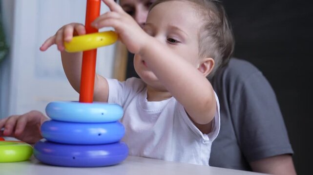 Baby stacking colorful ring stacker toy on pole with toddler reach and parent guide, child focused on play and learning, development of motor skill and coordination, hand exploration and curiosity