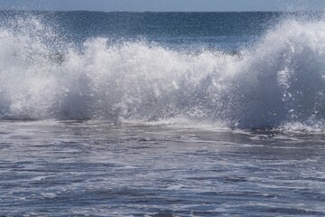 Dynamic ocean wave with foam and spray on the volcanic beach of Tenerife. Beautiful natural seascape showing strength, motion, and contrast of deep blue Atlantic water.