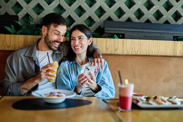 Portrait of ayoung romantic couple in restaurant having lunch and using a mobile phone