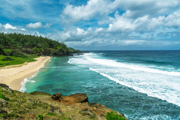 Panoramic view of a secluded tropical bay with white sandy beach and crashing turquoise waves under a dramatic cloudy sky