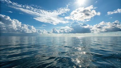 Fototapeta premium A serene ocean view under a bright sky, featuring calm waters reflecting sunlight and scattered clouds.