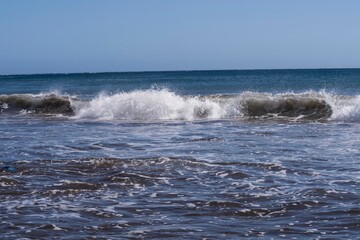 Dynamic ocean wave with foam and spray on the volcanic beach of Tenerife. Beautiful natural seascape showing strength, motion, and contrast of deep blue Atlantic water.