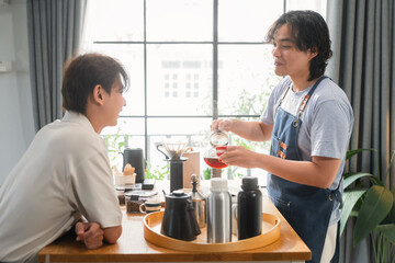 Asian mature man enjoys morning coffee at cafe using drip coffee bag in beige cup on white wood table, while young adult friends relax making specialty coffee as hobby activity at home	