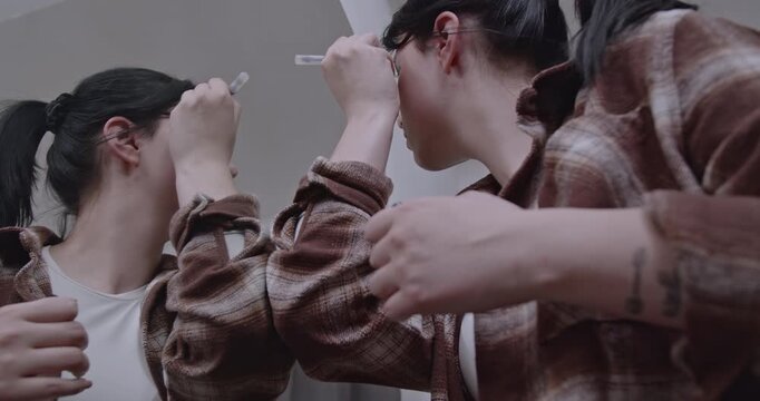Young woman applying makeup at home in front of a mirror, getting ready for the day. She carefully uses eyebrow gel to shape her eyebrows.