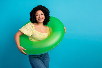 Charming woman holding inflatable pool float while smiling against blue background showcasing joy and summer vibes