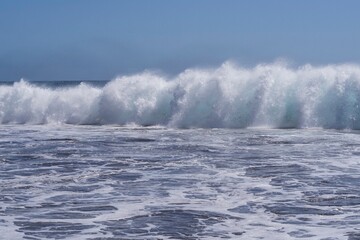 Strong waves breaking on the Atlantic shore near El Medano, Tenerife. Natural power and texture of sea water under clear blue sky — symbol of energy and motion.