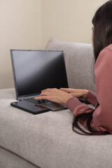 A young woman reclines on a comfortable sofa at home, looking at her laptop screen, relaxing in a casual, cozy environment, enjoying a peaceful and calm moment.