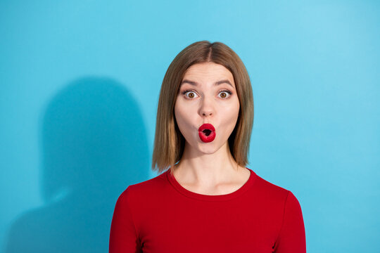 Young beautiful woman in red top expressing surprise with rounded lips against vibrant blue background