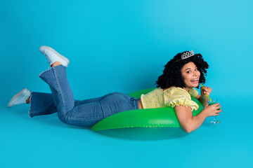 Charming young woman relaxing on an inflatable with a cheerful expression against a vibrant blue background, embracing positive vibes