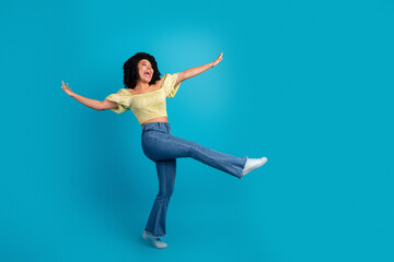 Obraz premium Joyful young woman with curly black hair expressing happiness in casual outfit on a bright blue background