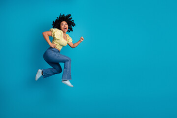 Joyful young woman with curly hair jumps on vibrant blue background showcasing playful energy and a casual stylish outfit