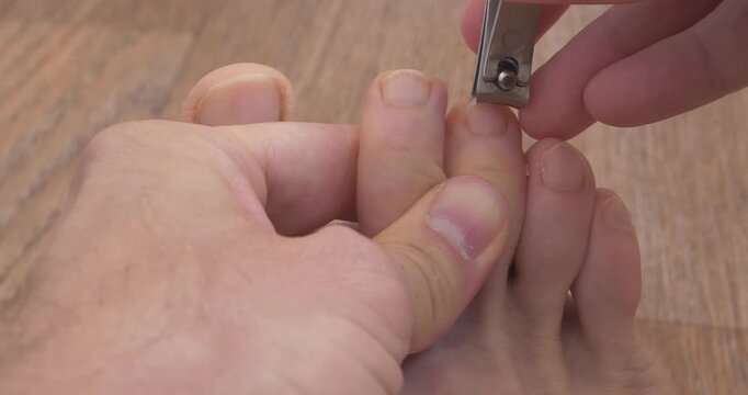A man cuts his toenails using metal nail clipper. Foot and toes of an adult man, close-up shot video
