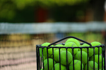 tennis balls collected in an iron rack with a tennis net in the background