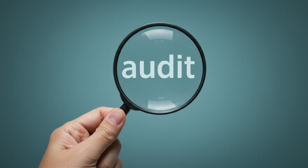 Hand holding magnifying glass over the word audit on textured background