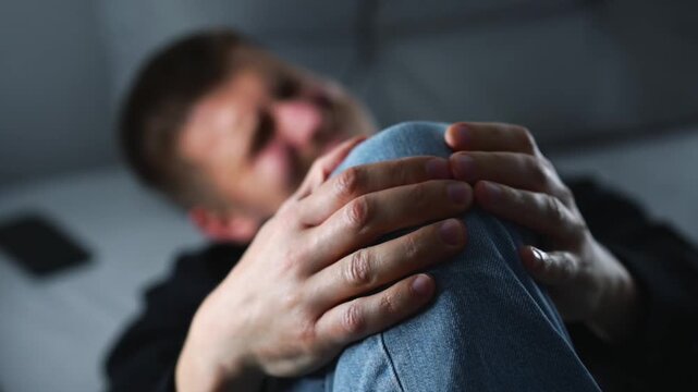 A young man screams in pain in his knee.
Arthritis and joint problems.
A man with a painful leg on a gray sofa