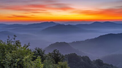 Obraz premium A scenic view of mountains covered in fog with a vibrant orange and pink sunset sky above them all
