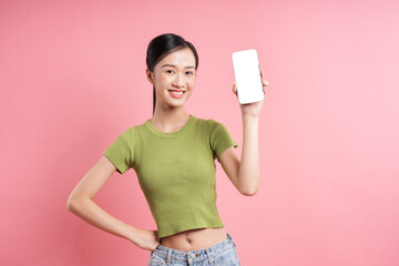 Cheerful woman presenting a phone with a blank screen against a vibrant pink backdrop