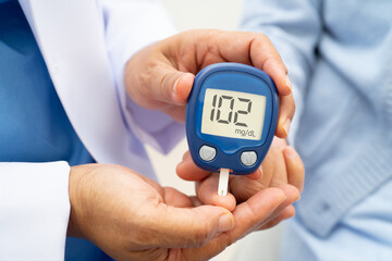 Asian doctor using digital glucose meter for check sample blood sugar level to treatment diabetes.
