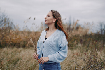 A candid outdoor portrait of a woman in a cozy cardigan standing in a windswept meadow, framed by...