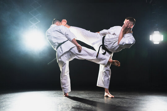 Martial arts masters on dark background. Strong man fighters in white kimono for karate martial arts fighting training in black gym. Karate fighters training punches kicks practicing fight sparring