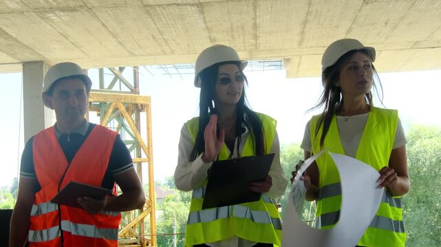 Cheerful worker and ladies managers walk through building. Specialists examine floor plan and evaluate results of tasks in special area
