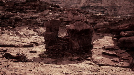 In the fading light of dusk, a striking rock formation rises from the sandy ground in a vast desert. Surrounding cliffs loom overhead, creating a sense of ancient mystery and isolation.