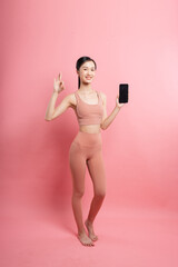 Smiling woman in athletic wear against a pink background making an OK gesture with her hand