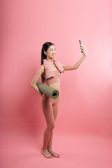 Woman in sportswear takes a selfie with a rolled-up mat against a pink background