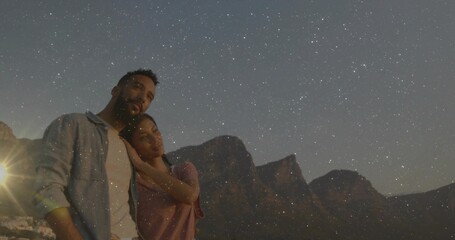 Couple cuddling on hillside, gazing at rocky peaks and distant lights under lamp glow, copy space