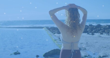 Standing woman wearing striped swimsuit gazing toward horizon at tidal pool, with volcanic rocks
