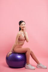 Enthusiastic young woman in sporty outfit smiles and waves while perched on an exercise ball