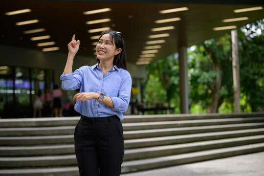 Asian businesswoman pointing up, having an idea outdoors