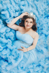 pregnant girl lies on a blue background. girl in a blue dress. girl with a diamond crown. High quality photo