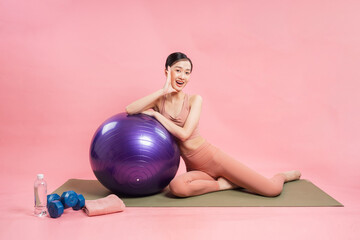 Fit and fabulous! Young woman enjoys a workout with stability ball on pink background