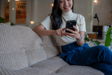 Asian woman smiling and relaxing on sofa using smartphone