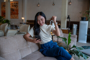 Obraz premium Asian woman celebrating success using smartphone in cafe