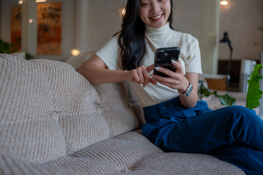 Asian woman smiling and relaxing on sofa using smartphone