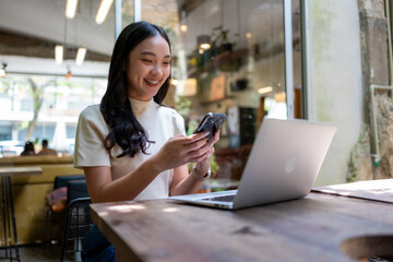 Asian woman remote working from cafe on laptop and smartphone