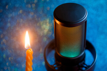 Pro condenser microphone with RGB glow beside a lit spiral candle on shimmering blue bokeh, evoking a cozy Christmas podcast or live stream mood. Photo