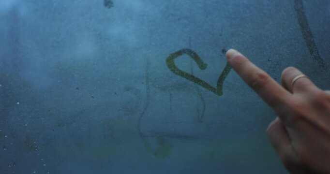 Person draws a heart shape on a foggy, rainy car window. Creative, moody, and contemplative moment symbolizing love and connection on a rainy journey.